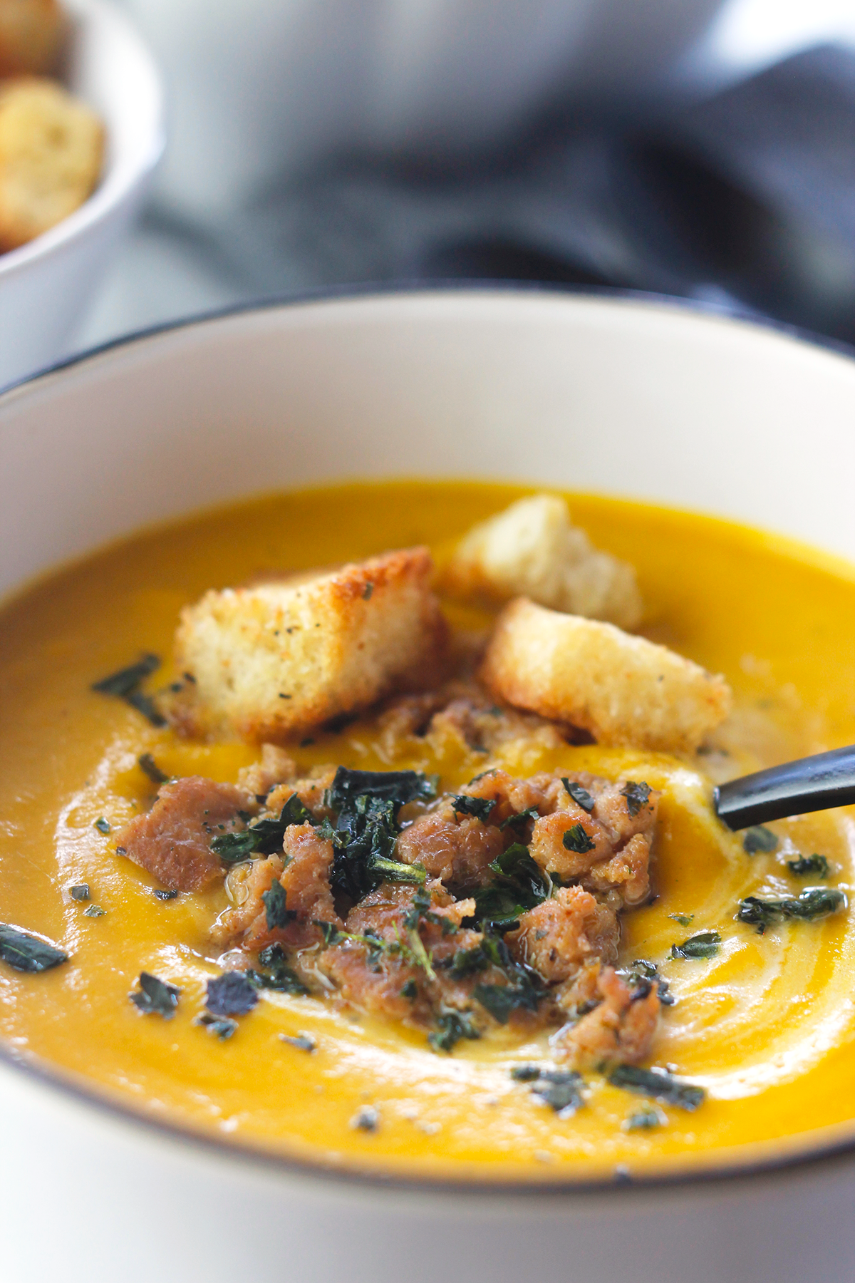 A very close-up shot of butternut soup a bowl, topped with sweet italian turkey sausage, chopped parsley and 3 crouton