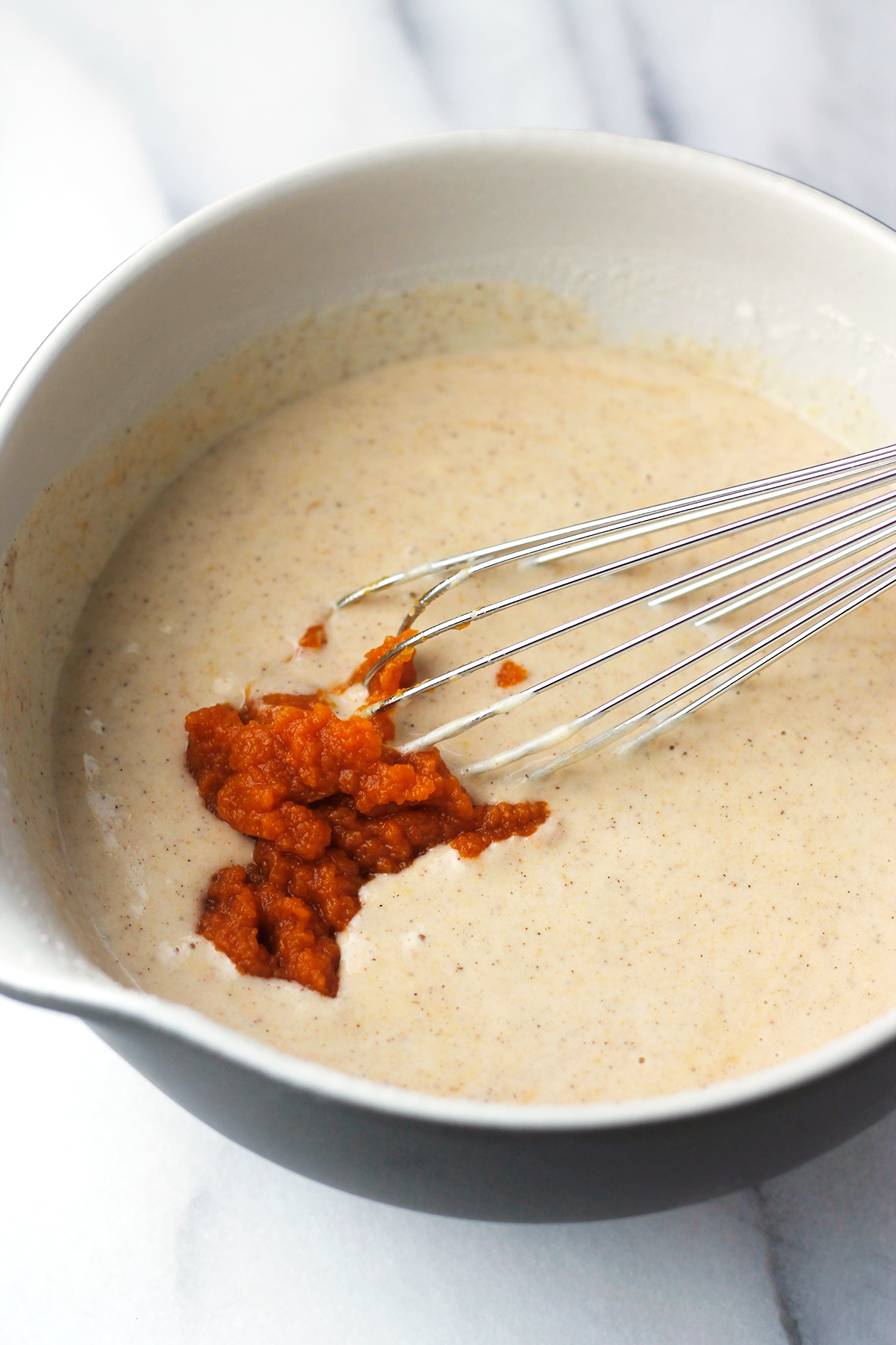 Bowl of pumpkin pancake batter with pumpkin puree and a whisk.