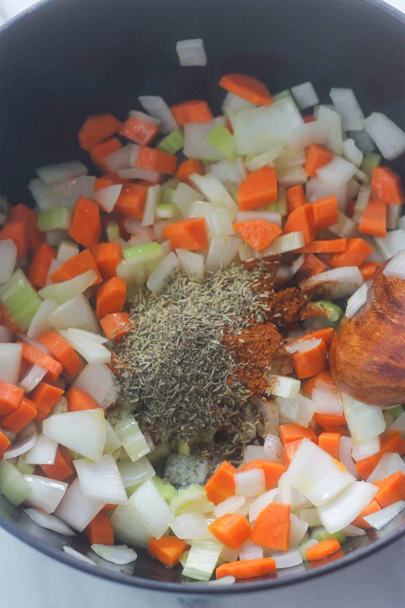 Overhead shot of onions, celery, carrots with herbs and spices sautéing in pot.