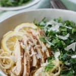Overhead shot of lemon pasta with sliced grilled chicken and chopped arugula and a plate of more chopped arugula in the background.