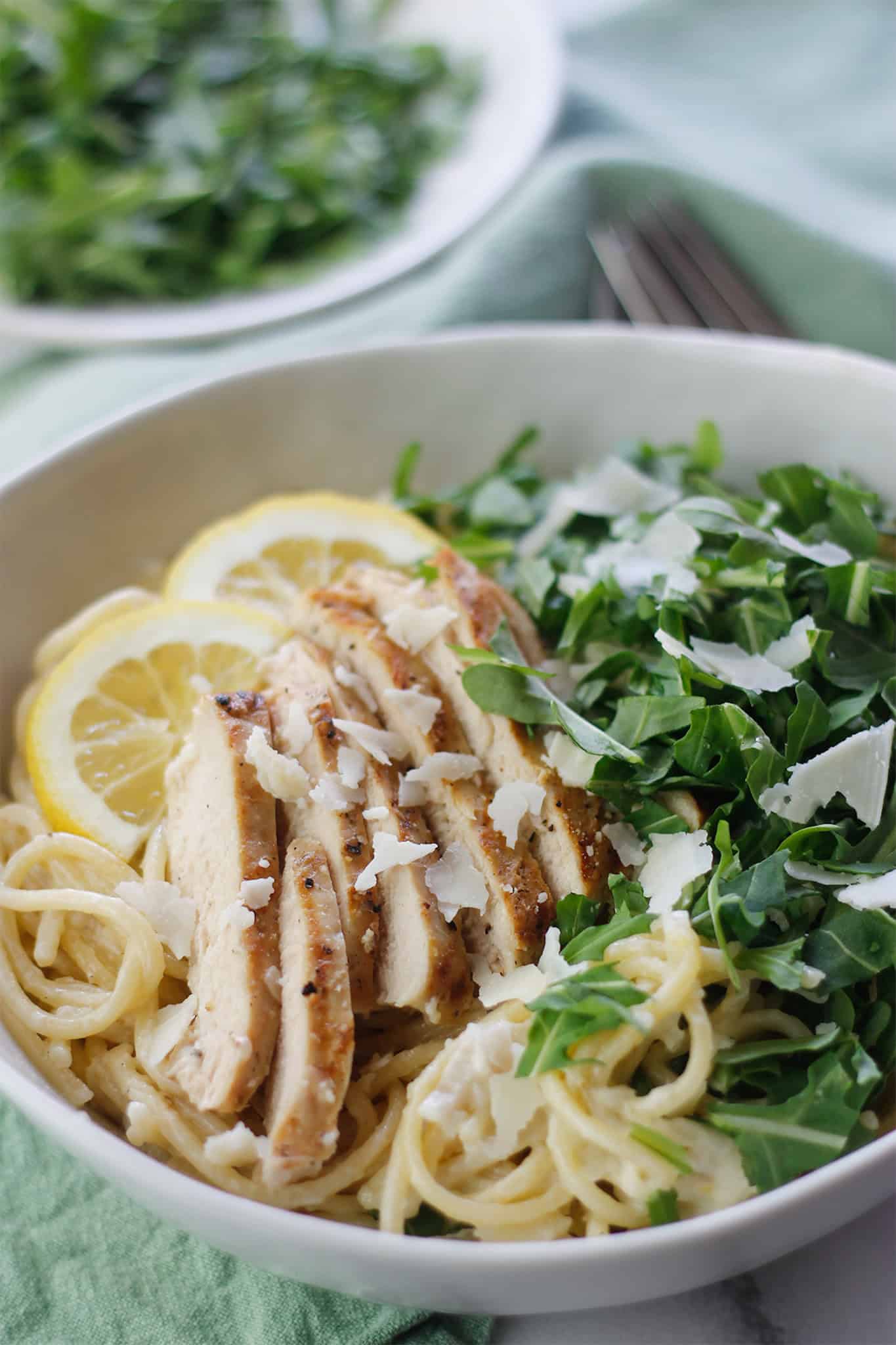 Close-upangle shot of pasta grilled chicken and arugula in white bowl.