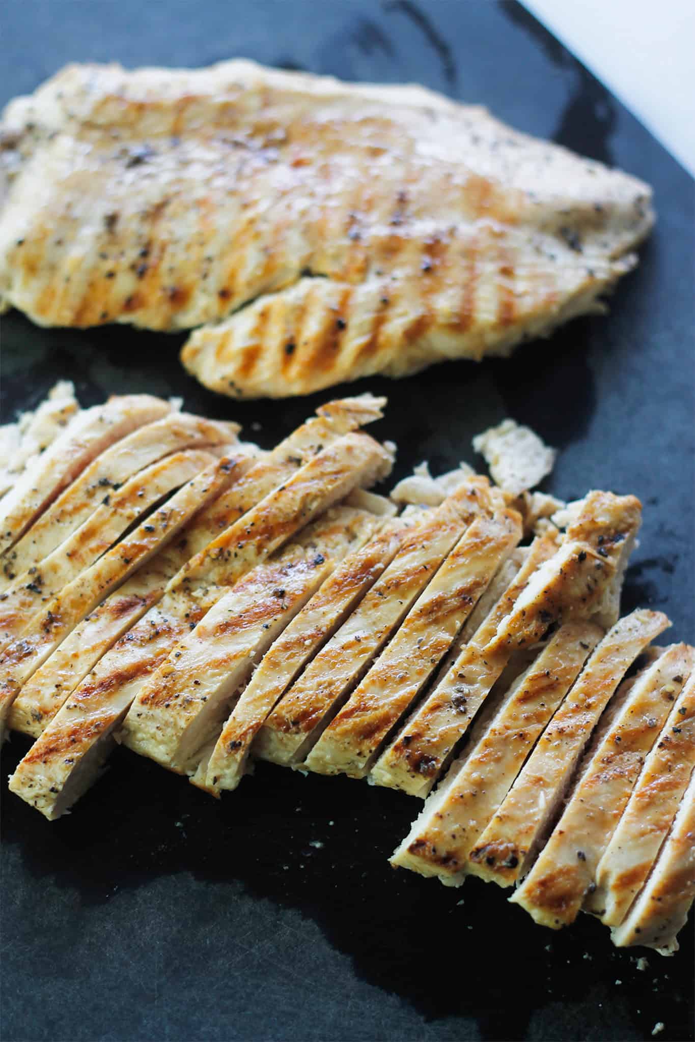 Sliced grilled chicken breast on cutting board.
