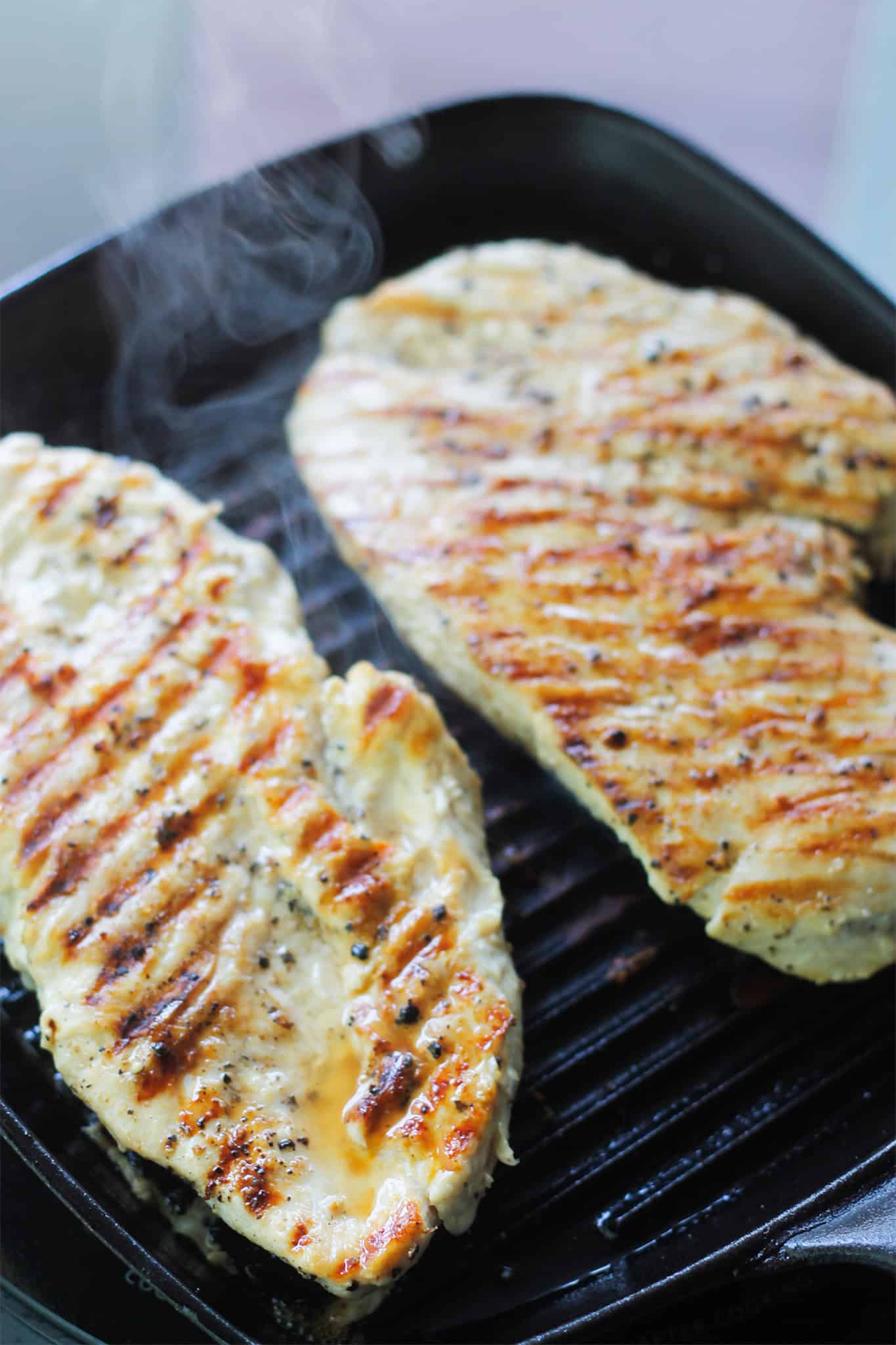 Two chicken breast cooking on grilled pan.