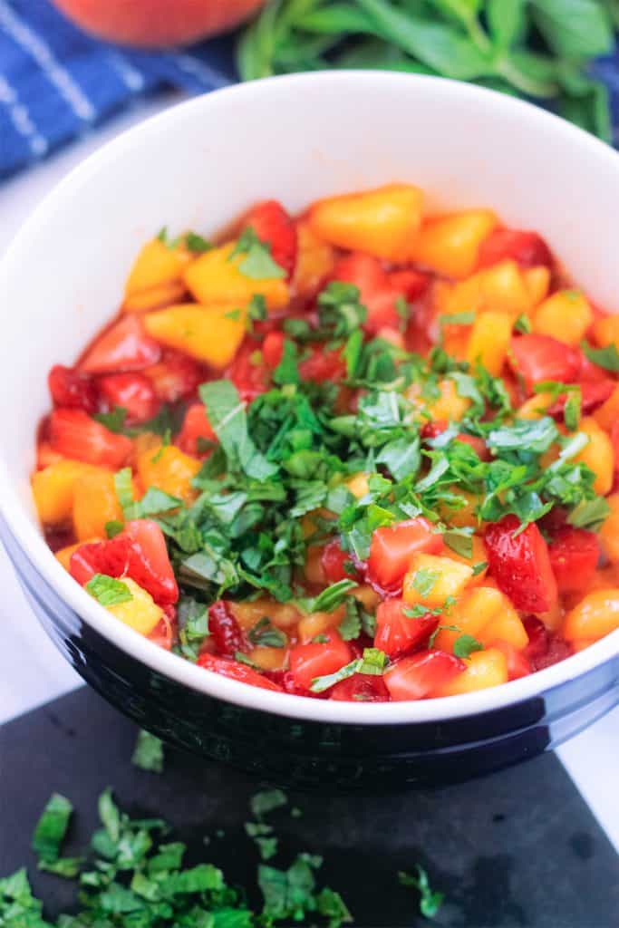 Bowl of diced strawberries and peaches topped with chopped mint and basil.