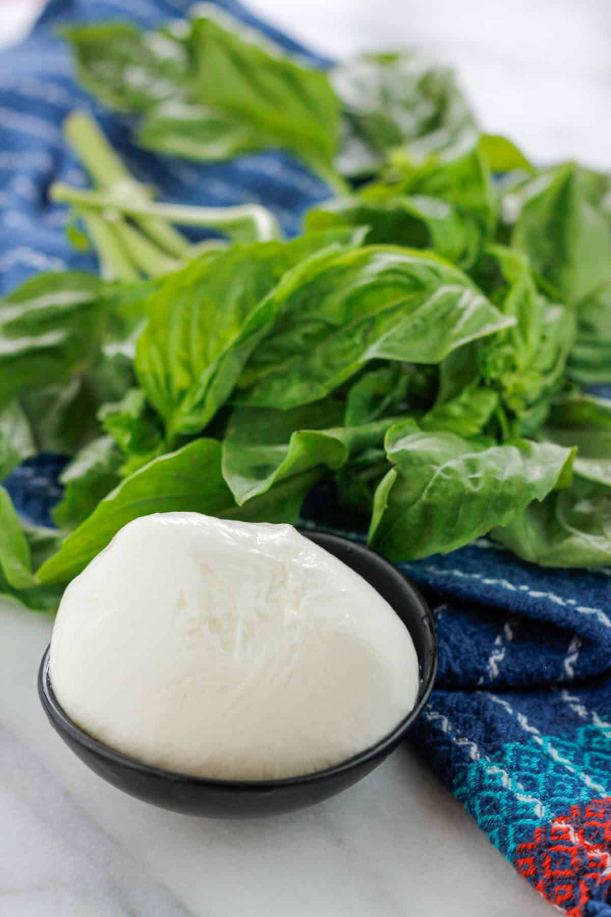 Fresh ball of Burrata in a small bowl with a fresh bunch of basil on blue kitchen towel