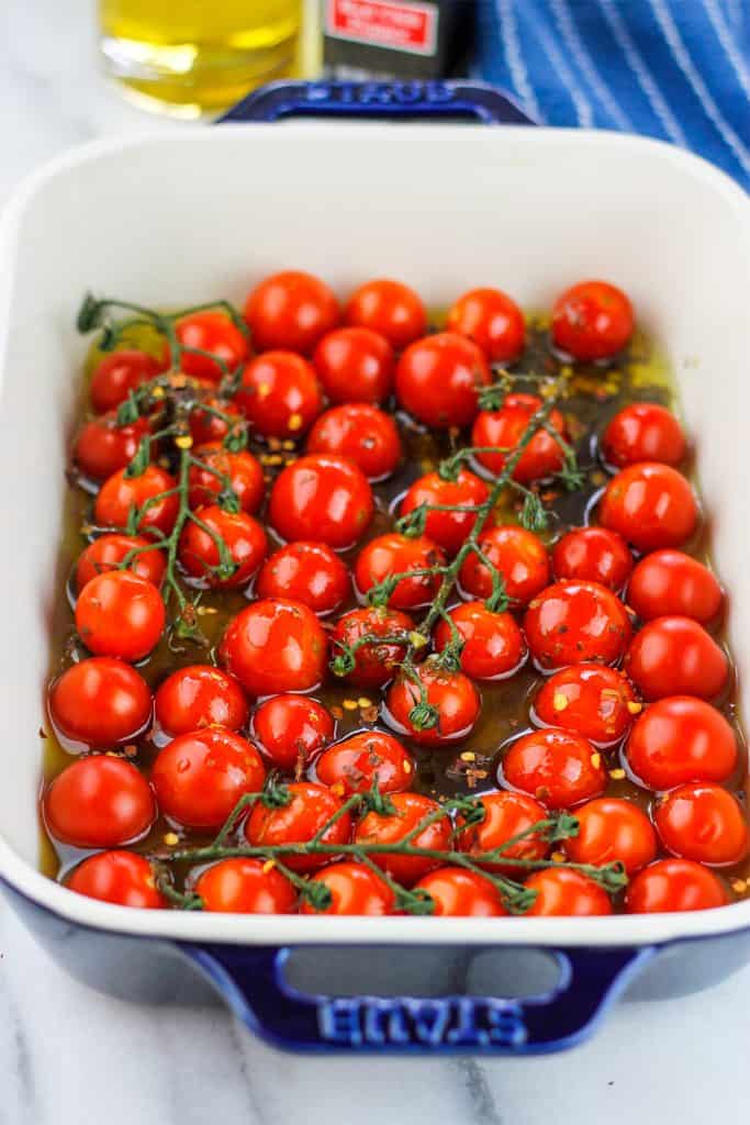 Cherry tomatoes in rectangle baking dish with olive oil poured over the tomatoes