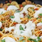 Close-up of sausage pasta with torn burrata scattered over the top and fresh torn basil leaves.