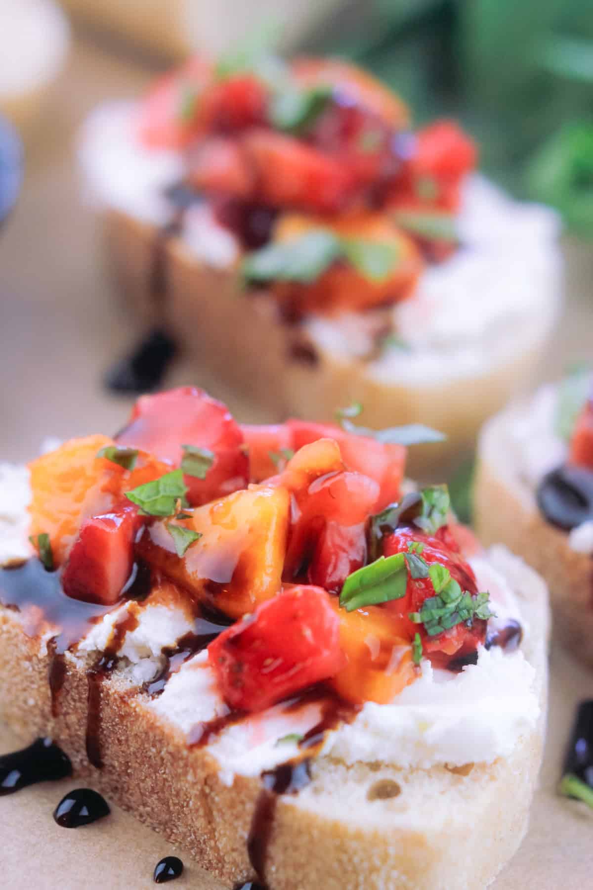 Close-up shot of prepared strawberry and peach bruschetta drizzles with honey and balsamic glaze and sprinkled with chopped mint and basil.
