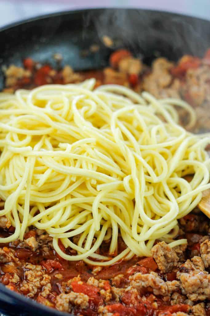 Cooked pasta on top of sausage and tomatoes in a large skillet.