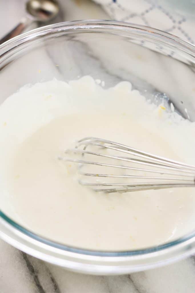 Lemon cream cheese topping in a glass mixing bowl being whisked with a stainless steel whisk.