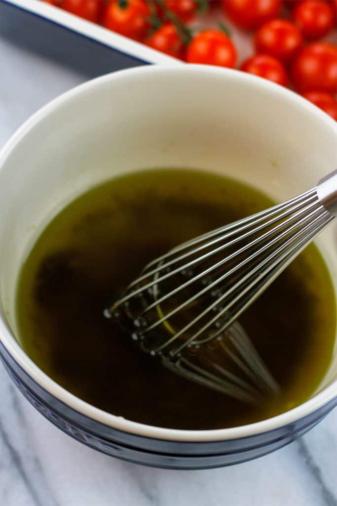 Overhead shot of olive oil and pesto mixture in a mixing bowl with a whisk