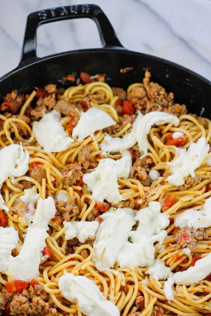 Overhead shot of skillet filled with sweet Italian sausage pasta with tomatoes and torn burrata scattered over the top of the pasta