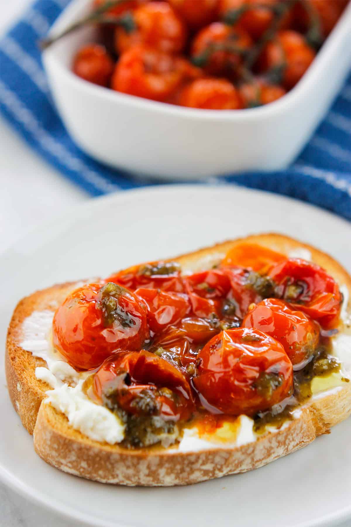 Roasted tomatoes on toast with a container of roasted tomatoes in the background.