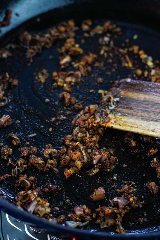 Sautéing shallots, garlic and spices in pan with a wooden spatula.