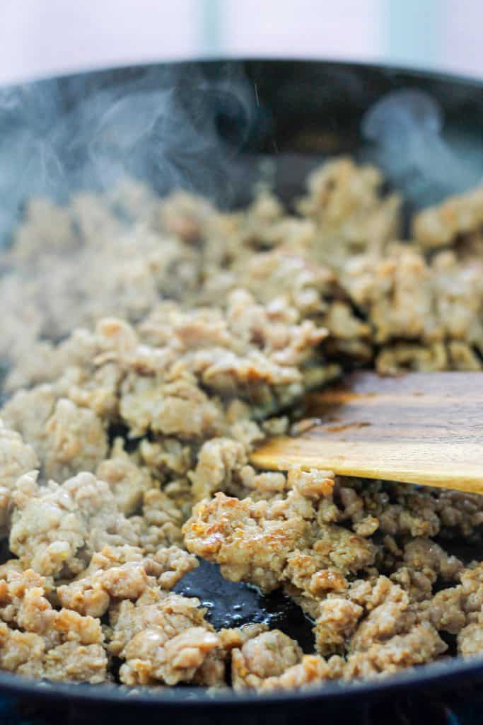 Italian sausage sauteein in skillet being stirred with a wooden spatula.