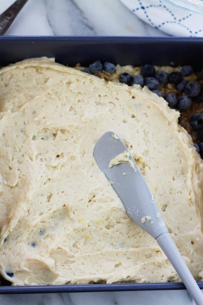 Second layer of crumb cake batter being spread over blueberry layer.