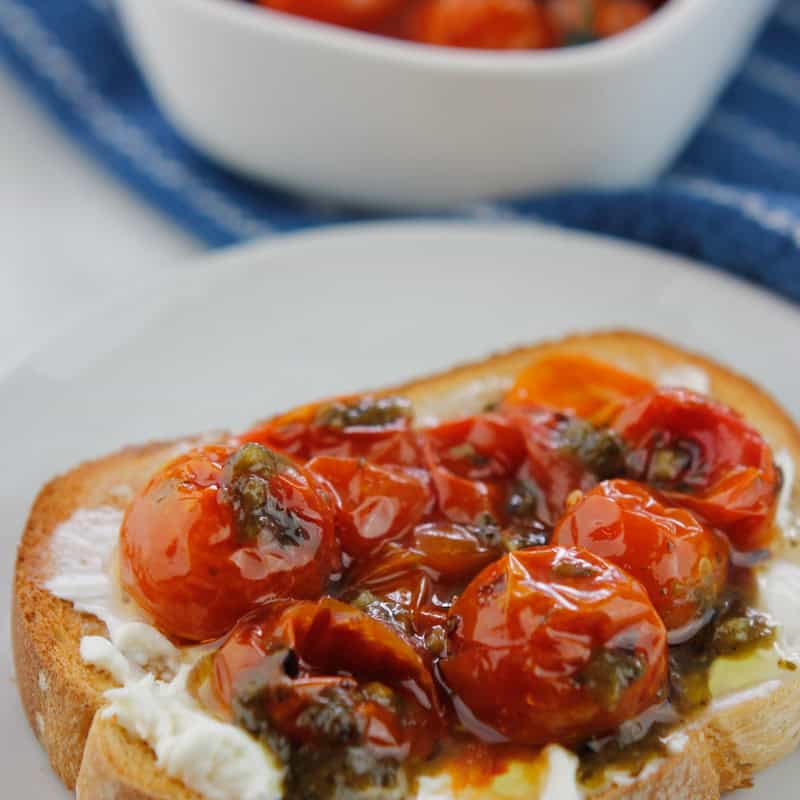 Roasted tomatoes on toast with a container of roasted tomatoes in the background.