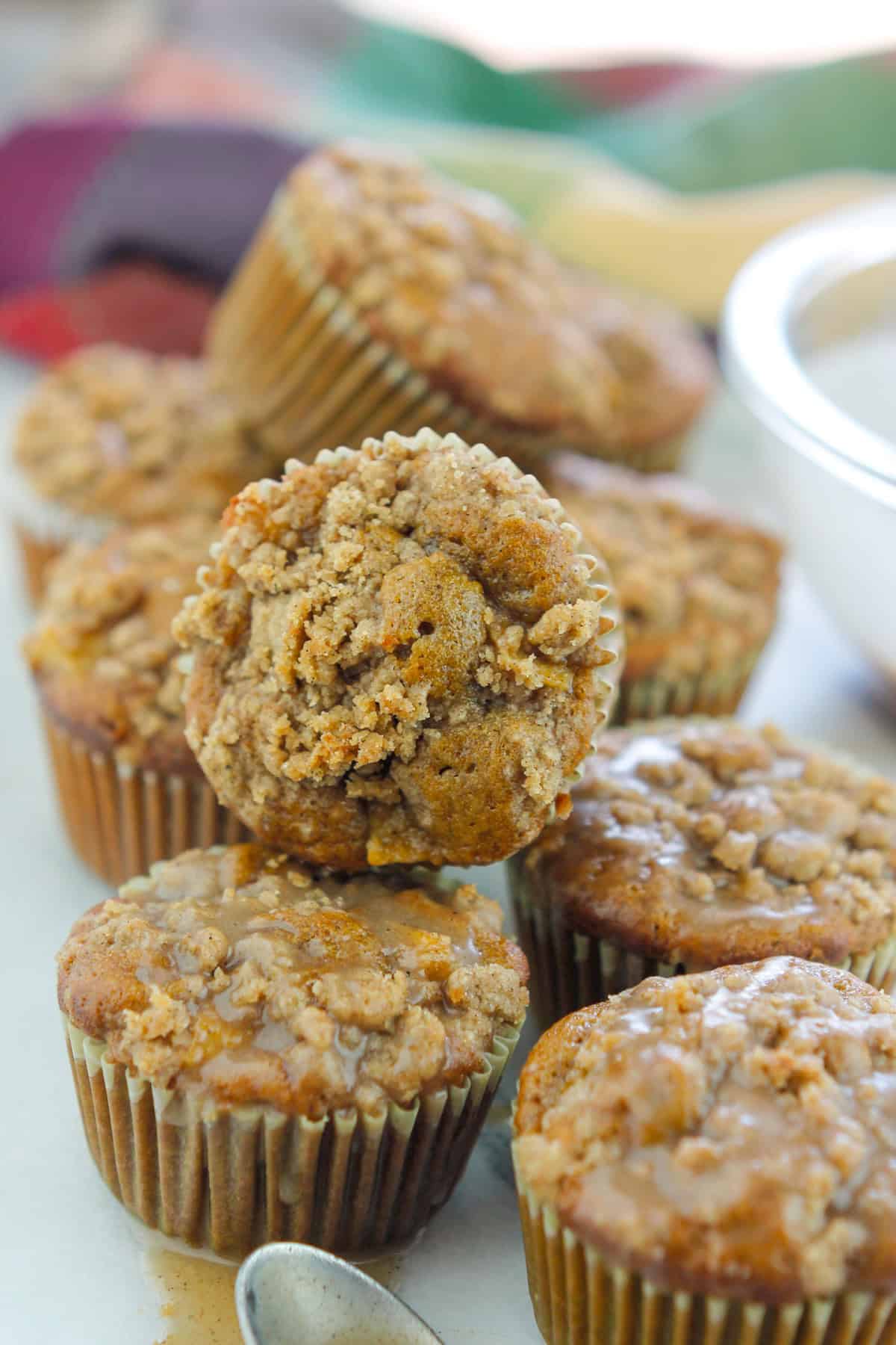 Batch of Chai Apple muffins on counter with a small spoon in front of muffins with chai sugar glaze on spoon.