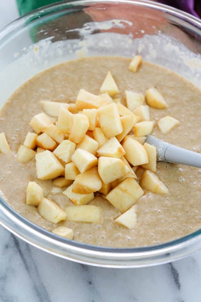 Bowl of chai apple muffin batter with diced apples on top with spatula in the bowl.