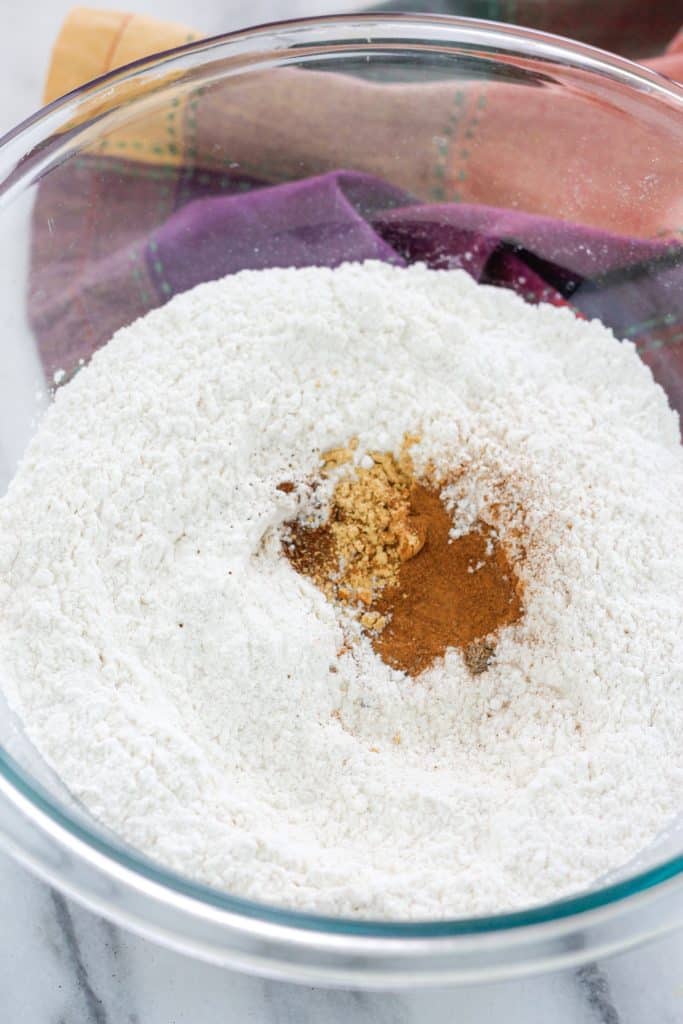 Clear glass mixing bowl with dry ingredients in the bowl with the chai spices on top of the dry flour mixture.