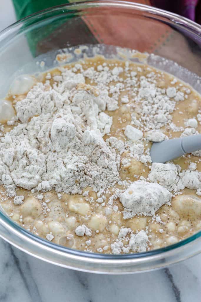 Dry ingredients being mixed into wet ingredients in a bowl with spatula in the bowl.