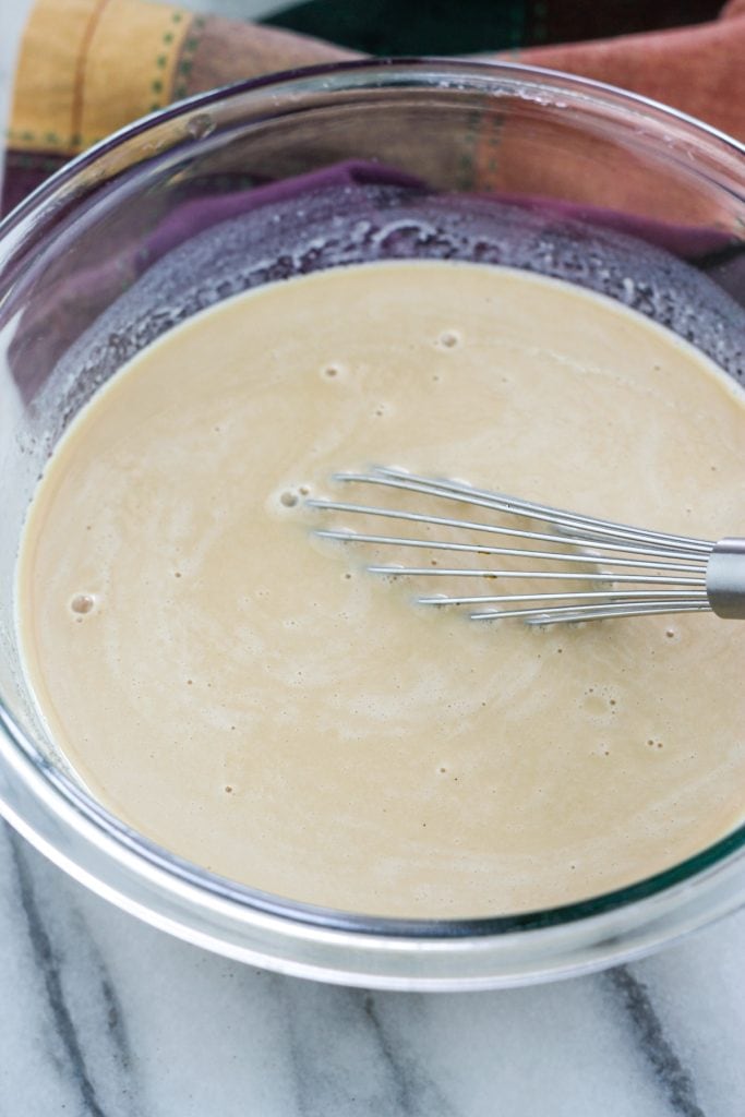 Glass bowl filled with all the wet ingredients mixed together with a wire whisk.