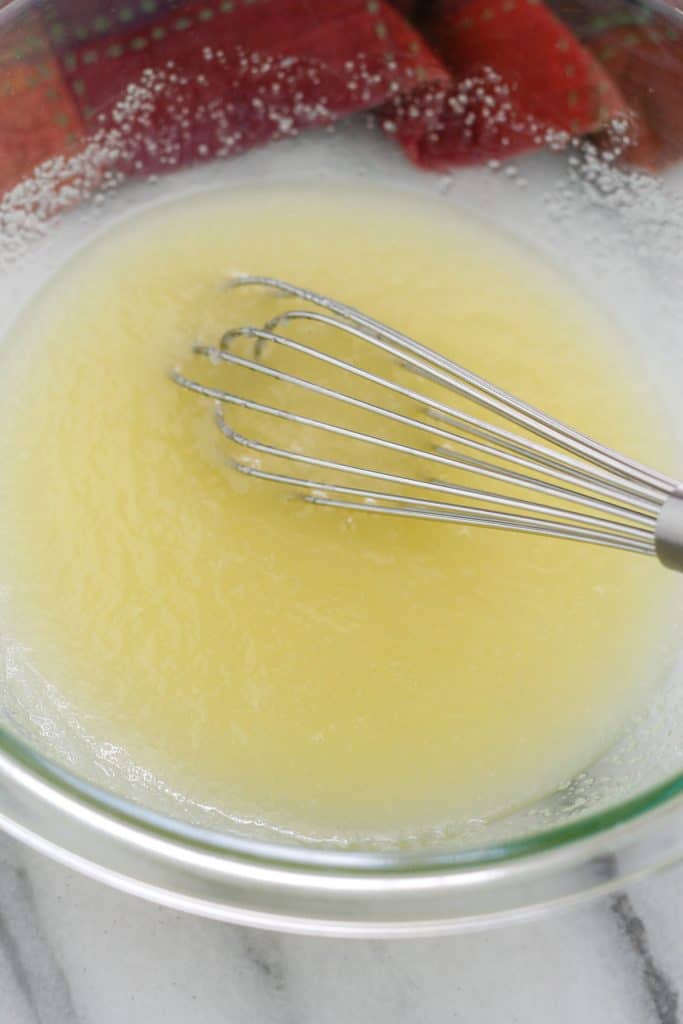 Glass bowl with sugar and butter mixed together with a whisk.