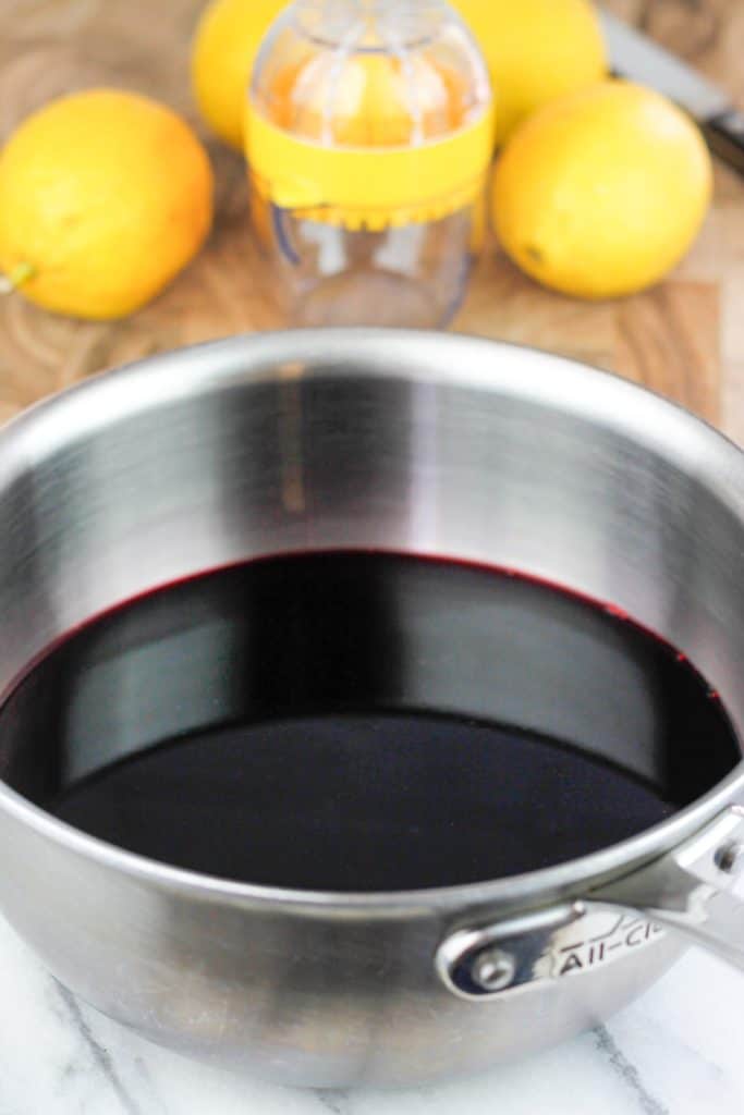 Hibiscus tea mixed with sugar in a pot with lemons on cutting board in the background.