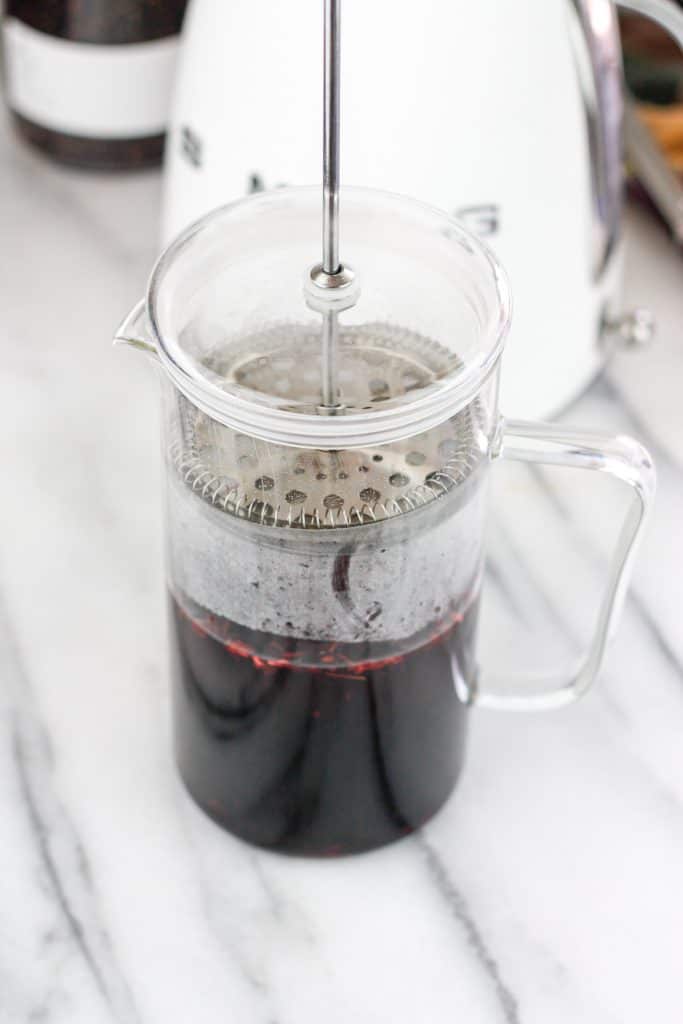 Loose leaf hibiscus tea steeping in a french press with a SMEG electric kettle in the background.