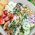 Overhead shot of bowl filled with Mediterranean grain bowl salad with a bunch of fresh flat leaf parsley at the top right corner of the bowl.