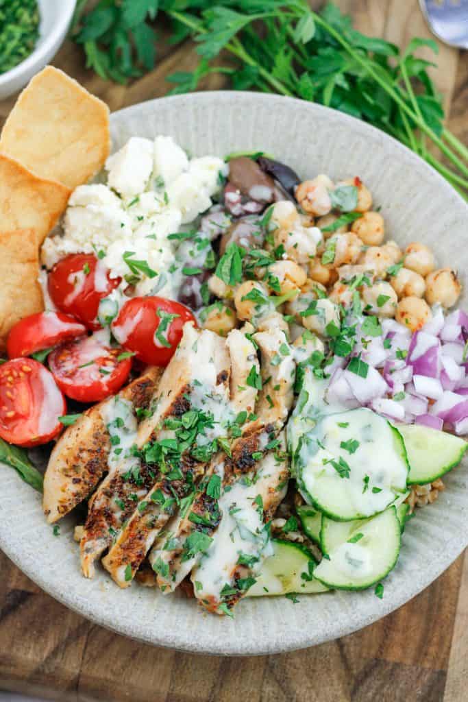 Overhead shot of bowl filled with Mediterranean grain bowl salad with a bunch of fresh flat leaf parsley at the top right corner of the bowl.