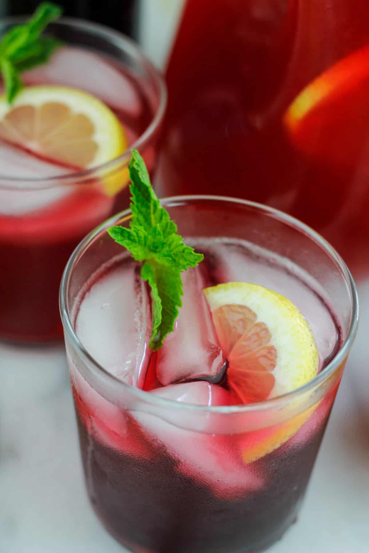 Overhead shot of hibiscus lemonade made with hibiscus syrup garnished with sliced lemon and fresh mint in a short glass.