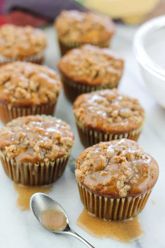 Shot of chai apple muffin on counter with the front muffins topped with some of the chai glaze with a small spoon filled with chai sugar glaze.