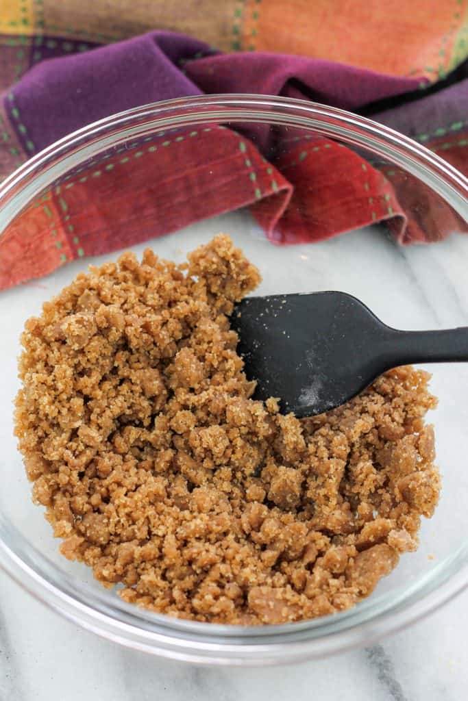 Shot of crumble mixture in a small glass mixing bowl with a dish towel in the background.