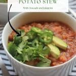 Bowl of spicy lentil sweet potato stew garnished with sliced avocado and jalapeños.