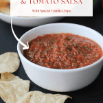 Roasted tomatillo and tomato salsa in a white bowl with tortilla chips to the left of the bowl of salsa.