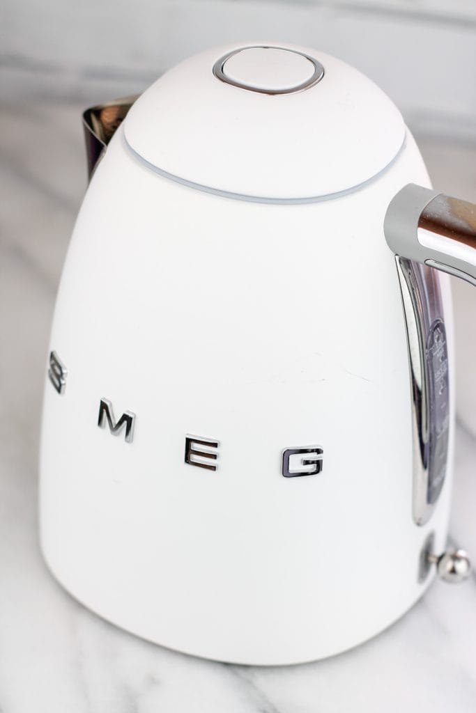 White SMEG electric kettle on a marble countertop.