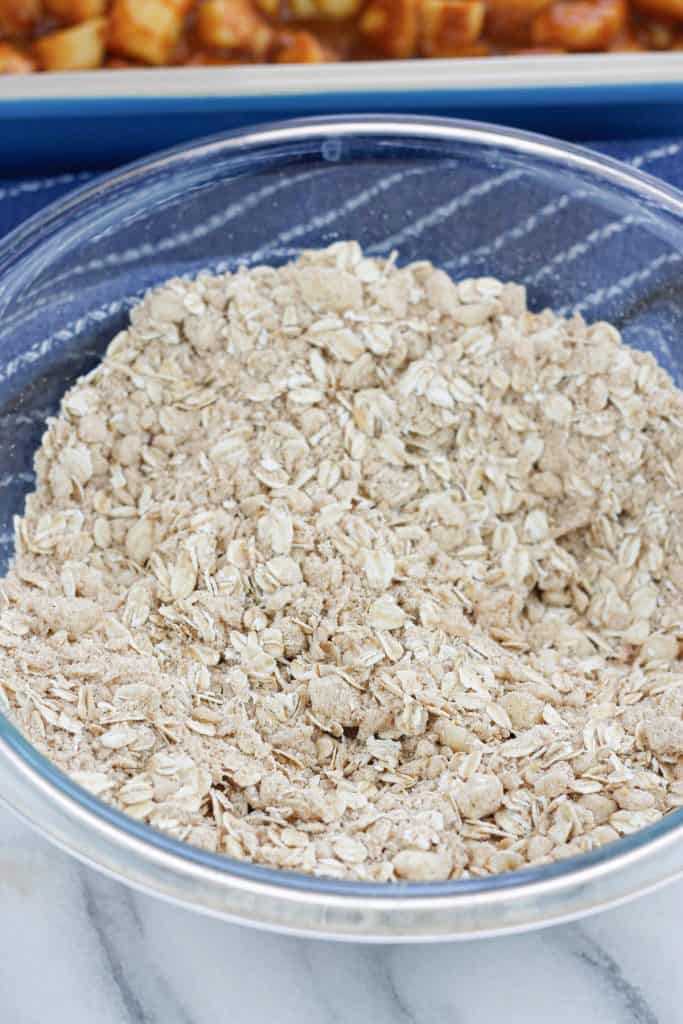 Apple crisp topping with the oats mixed with the flour in a clear glass bowl.