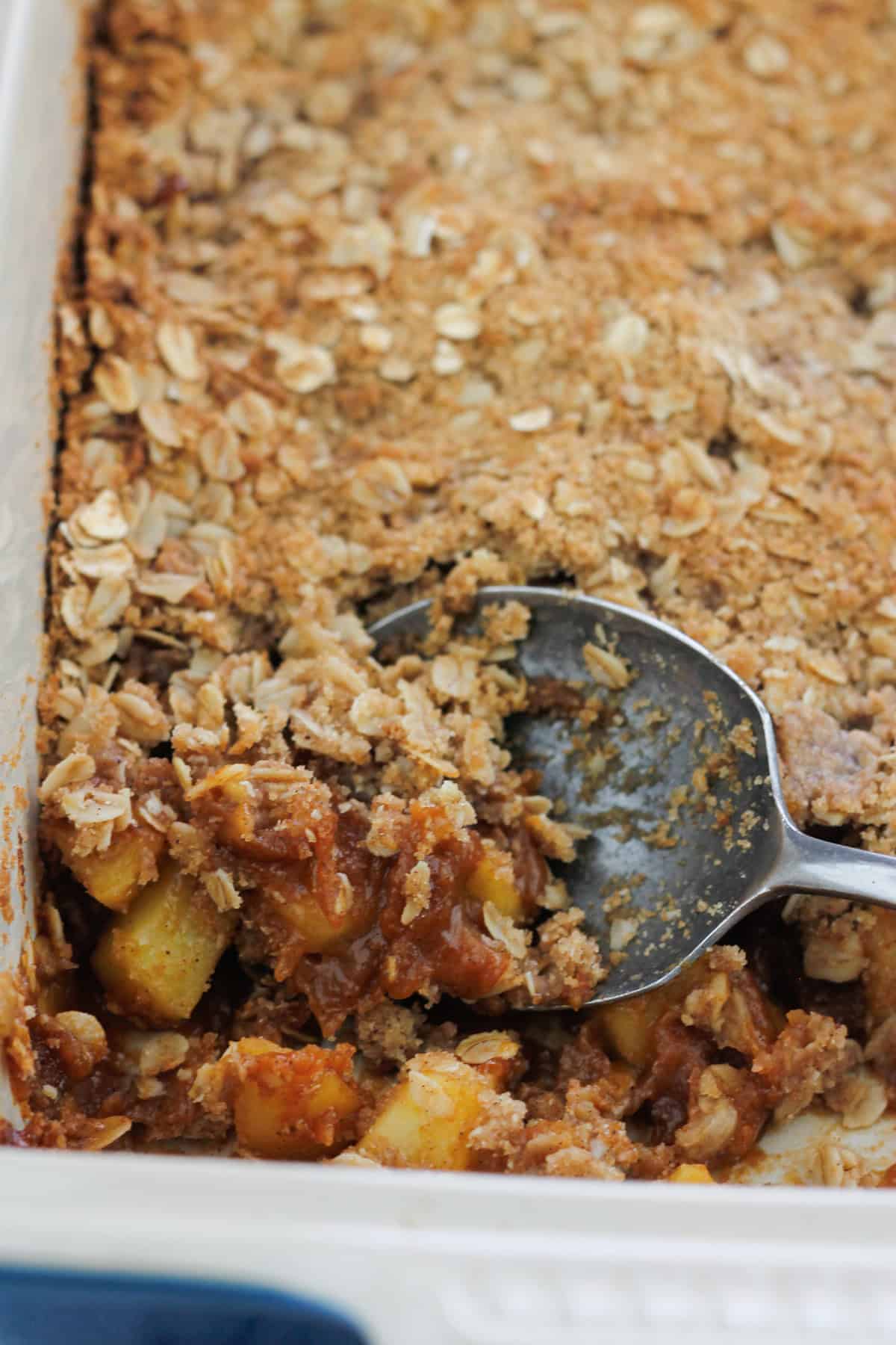 Baked apple crisp being scooped out of the baking dish with a metal spoon.