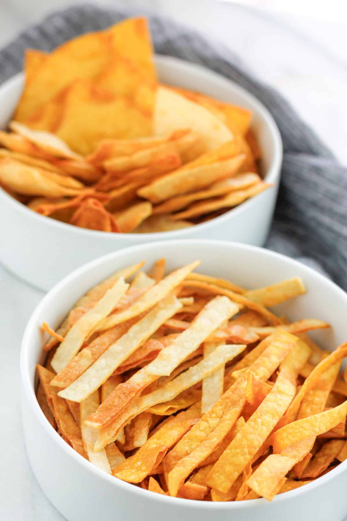 Crispy fried tortilla strips in a bowl with a bowl fried tortilla chips in the background.