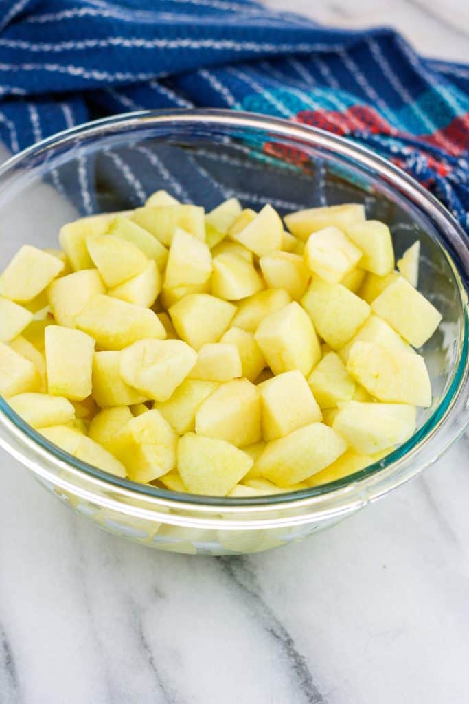 Diced apples in a glass bowl with a blue stripe dish towel behind the bowl of apples.