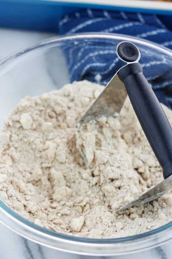 Flour, sugar, and butter in a clear glass bowl with a pasty cutter in the bowl.