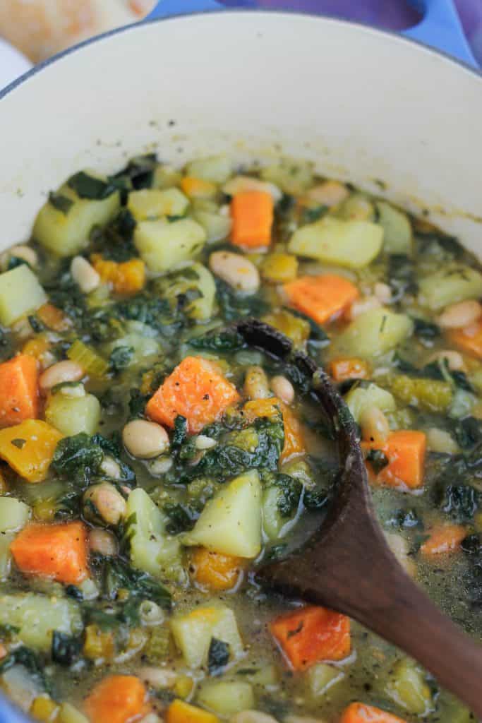 Overhead shot of butternut white bean soup with Swiss chard in dutch oven with a wooden spoon.