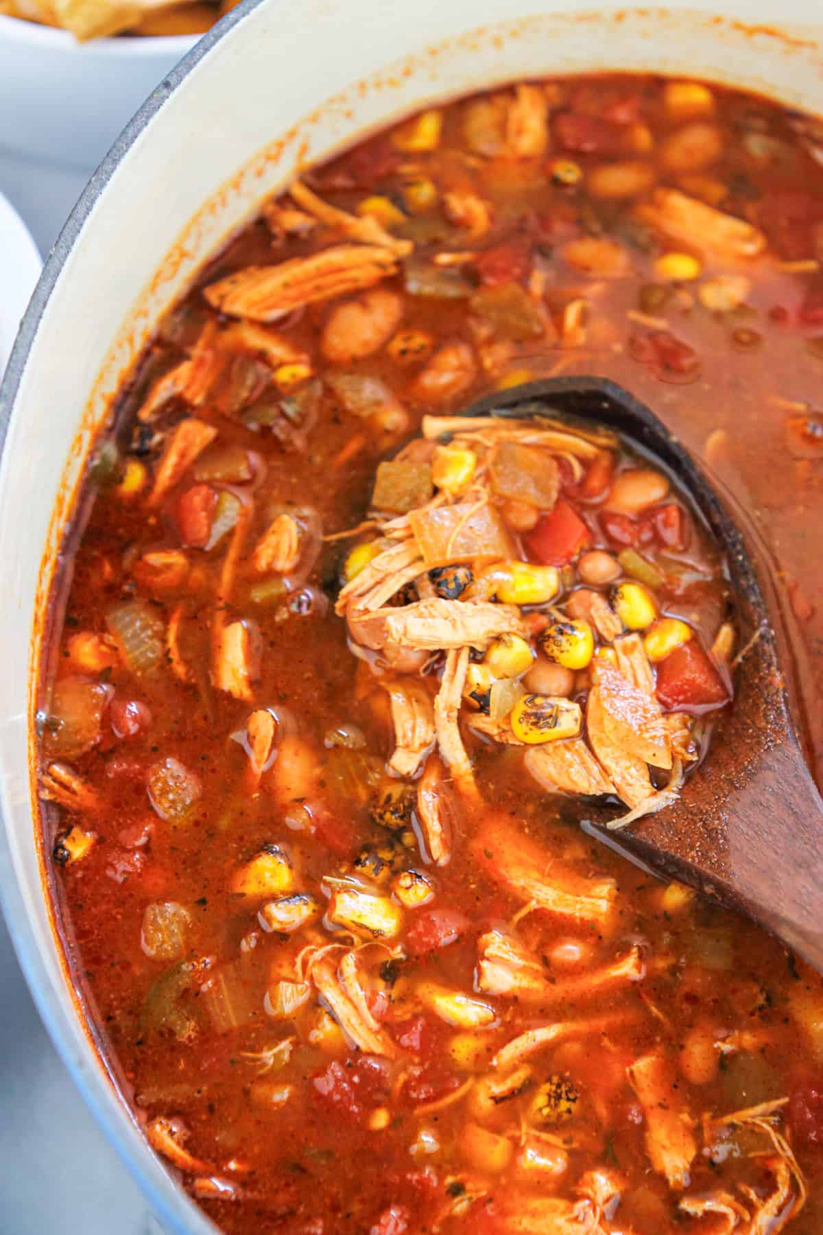 Overhead shot of easy rorisserie chicken tortilla soup in a dutch oven with a wooden ladle in the pot.