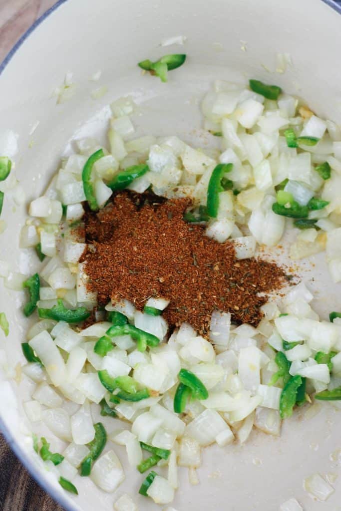 Overhead shot of chopped onions and jalapenos with taco seasoning in dutch oven.