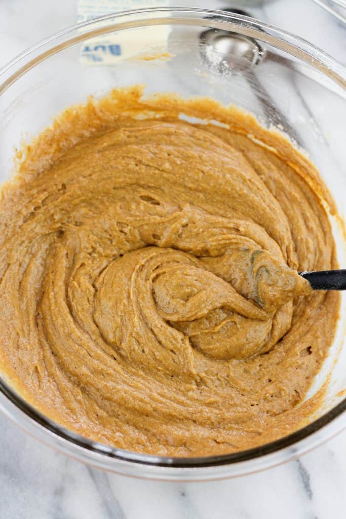 Pumpkin donut batter in a glass bowl with a spatula in the bowl.