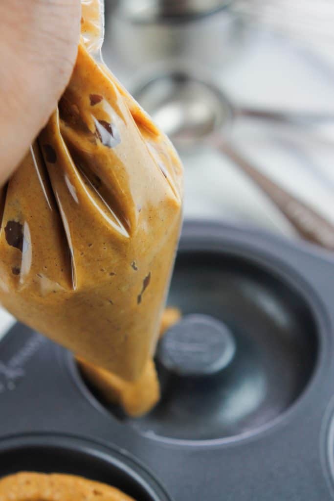 Pumpkin donut batter in a zip bag being piped into the donut pan.