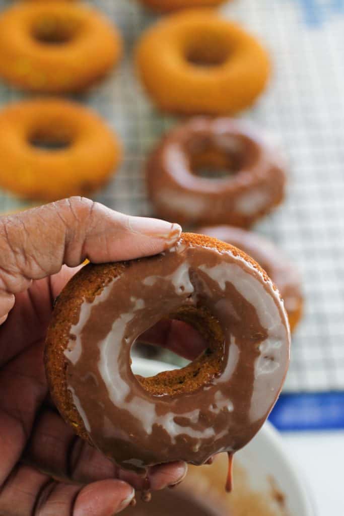 Pumpkin donut dipped in chocolate with the remainder of the baked donuts on a rack in the background.