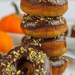 Stacked chocolate topped pumpkin donuts stacked on a plate with one donut propped on the stacked donuts.