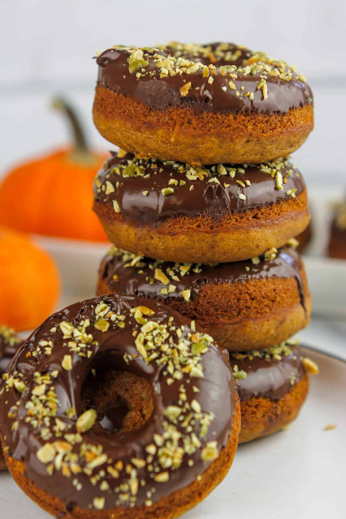 Stacked chocolate topped pumpkin donuts stacked on a plate with one donut propped on the stacked donuts.